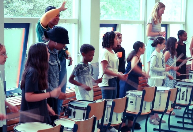 Rekenritmes - klas met basisschoolleerlingen met drumstokjes in hun handenvoor stoelen met drums