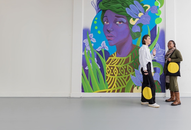 Twee personen met SKVR-tassen met gele cirkel voor een witte muur met kleurrijk schilderij