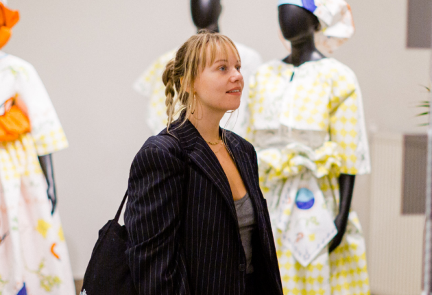 Een vrouw bekijkt een mode-expositie met kleurrijke jurken op mannequins.